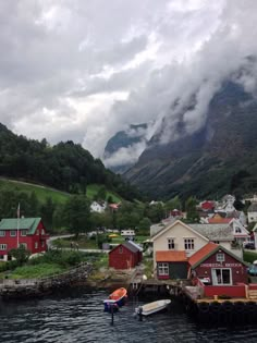 a small village on the water with mountains in the background and clouds rolling over it