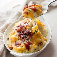 a spoon full of cheesy potatoes with bacon on top is being lifted from the casserole dish