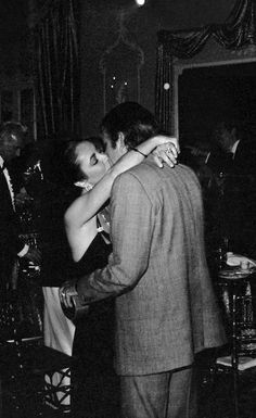 black and white photograph of two people dancing in a room with other people standing around