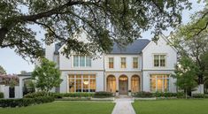 a large white house with lots of windows and trees in the front yard at dusk