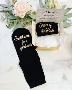 two pairs of black socks with gold lettering on them sitting in a box next to flowers