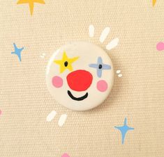 a button with a clown face and stars on the side, in front of a beige background