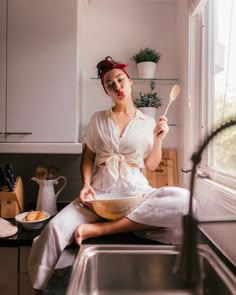 a woman sitting on the kitchen counter with a bowl and spoon in her hand