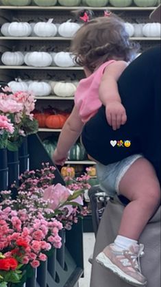 a woman holding a baby in her arms near some pink flowers and other colorful plants