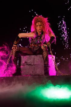 a woman with pink hair sitting on top of a wooden box in front of purple and green lights