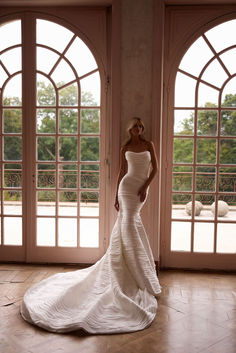 a beautiful woman in a white dress standing next to two large open doors and looking at the camera