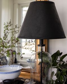 a lamp that is on top of a table next to a bowl and potted plant