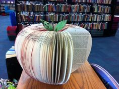 an apple shaped book sitting on top of a wooden table in front of a bookshelf