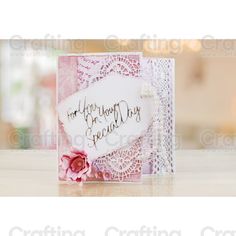 a close up of a card on a table with a pink flower in the middle