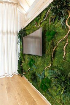 a tv mounted to a wall covered in green plants