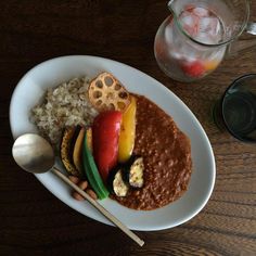 a white plate topped with meat and rice next to a glass of water on top of a wooden table