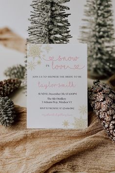 a white card with pink writing on it next to pine cones and snowflakes