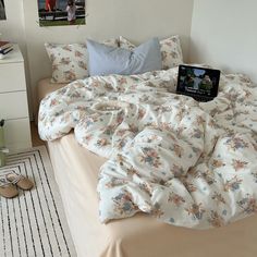 a laptop computer sitting on top of a bed covered in blankets and pillows next to two pairs of slippers