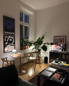 a living room filled with furniture next to a window covered in plants and pictures on the wall