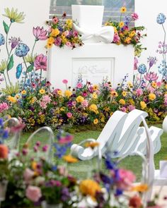 an arrangement of flowers and lawn chairs in front of a wall with a sign on it