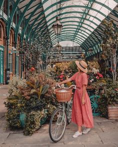 a woman in a pink dress and hat standing next to a bicycle with flowers on it