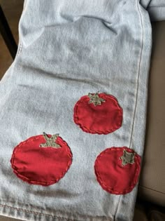 an old pair of jeans with red embroidered tomatoes on the front and back, sitting in a chair