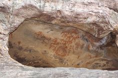 a cave with paintings on the side of it and rocks around it that have been carved into them