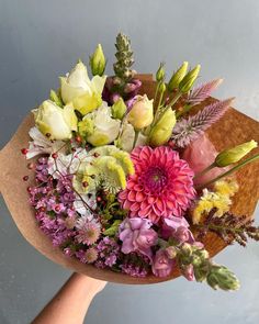 a bouquet of flowers sitting on top of a wooden table next to a person's hand