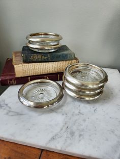 a stack of silver plates sitting on top of a marble table next to a book