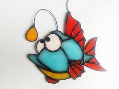 a stained glass fish ornament hanging from a chain on a white surface,