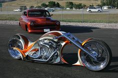 an orange and white motorcycle parked next to a red car on top of a parking lot