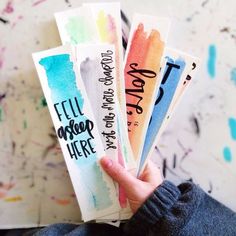 someone is holding four watercolor bookmarks in their left hand and the other one has writing on it