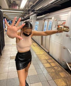 a woman wearing a mask and holding her hands up in the air while standing on a subway platform