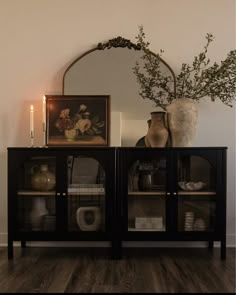 a vase with some flowers on top of it next to a glass doored cabinet