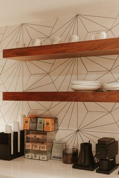 some shelves with coffee cups and other items on them in a home kitchen area that is decorated with geometric wallpaper