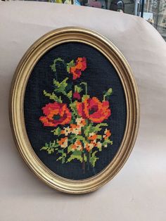 a cross stitched picture of flowers in a gold frame on a white tablecloth