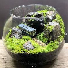 a glass bowl filled with green moss and rocks on top of a wooden table next to a small toy train