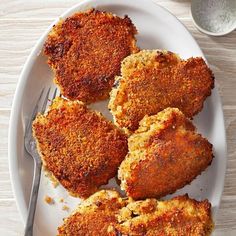 four pieces of fried chicken on a white plate with a fork next to the rest of the meal