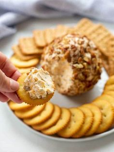 a hand holding a cracker with cheese and nuts on it next to crackers