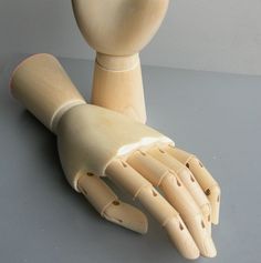 a wooden mannequin's hand and arm on a gray surface with a white wall in the background