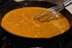 a skillet filled with sauce and whisk on top of a stovetop