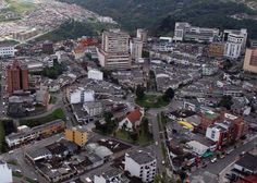 an aerial view of a city with lots of tall buildings and green hills in the background