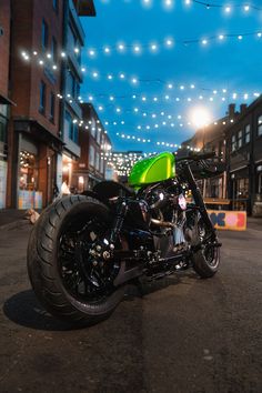 a green motorcycle parked on the street in front of some buildings with lights strung above it