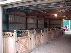 the inside of a barn with wooden stalls and horses in it's stall doors