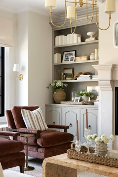 a living room filled with furniture and a fire place under a chandelier in front of a window