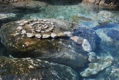 the rocks are surrounded by clear blue water and there is a rock with a circular design on it