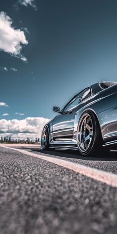 a silver sports car parked on the side of the road with clouds in the background