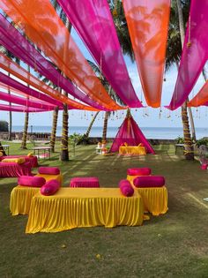 an outdoor wedding setup with pink and yellow linens on the grass near the ocean