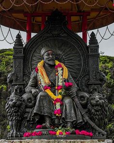 a statue of a man sitting on top of a chair with flowers around his neck