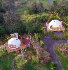 an aerial view of two white tents in the middle of a lush green field with trees