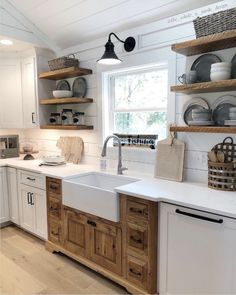 a white kitchen with wooden cabinets and open shelvings on the wall above the sink