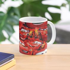 a mug with cars on it sitting on a table next to some books and a plant