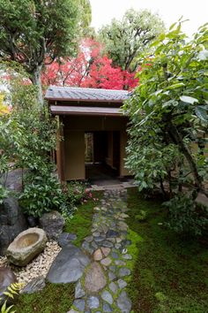 a small garden with rocks and trees in the foreground, along with a stone path leading to an outhouse