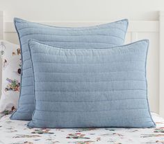 two blue pillows sitting on top of a bed next to a white headboard and pillow