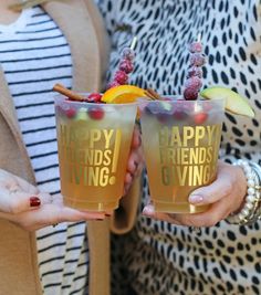 two women holding up glasses with fruit and herbs in them that say happy friends giving